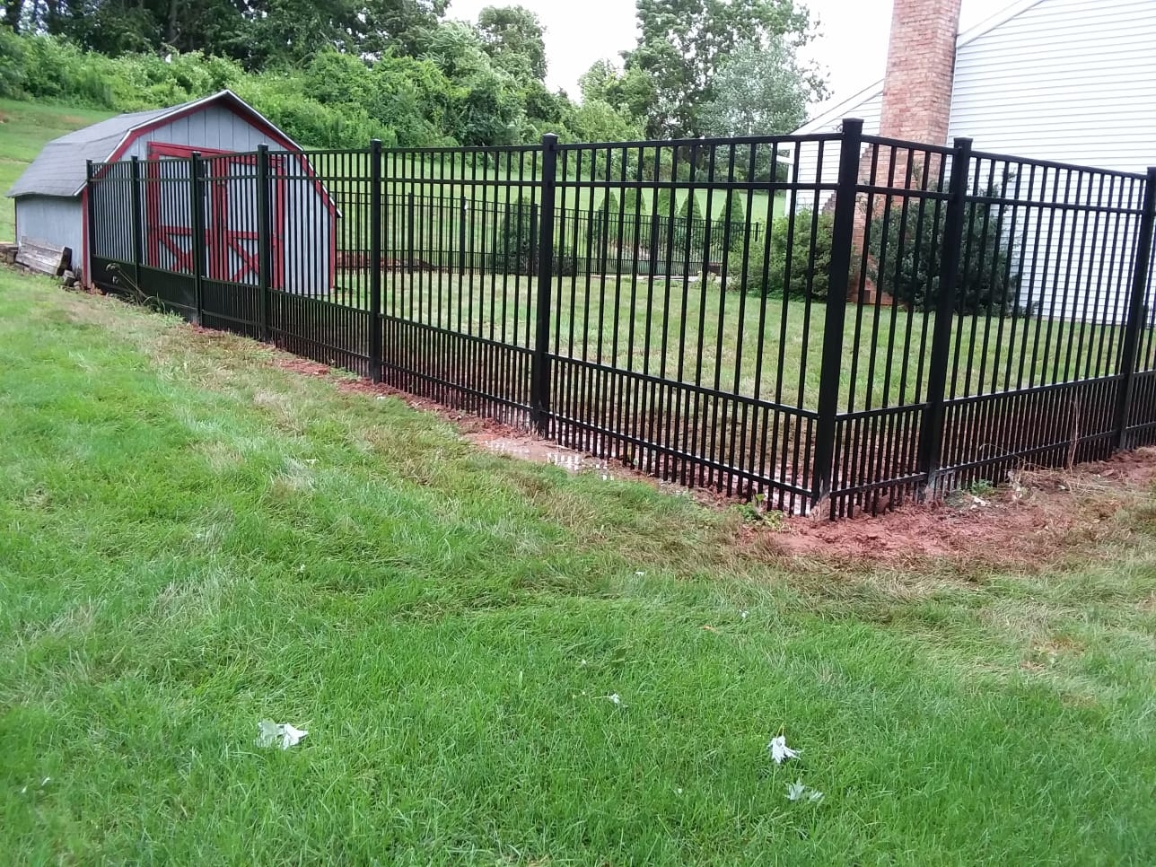 Black aluminum fence racked down a slope beside a barn on a residential property