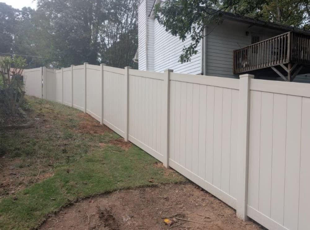 Tan vinyl privacy fence on a sloped yard in Cary NC with residential homes in the background