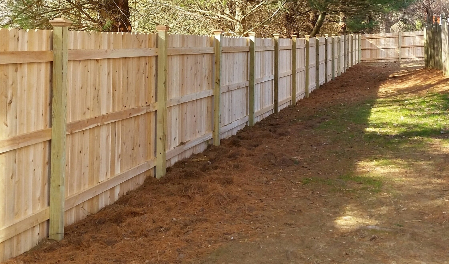 Long run of new pressure-treated dog-ear wood privacy fence with PT posts