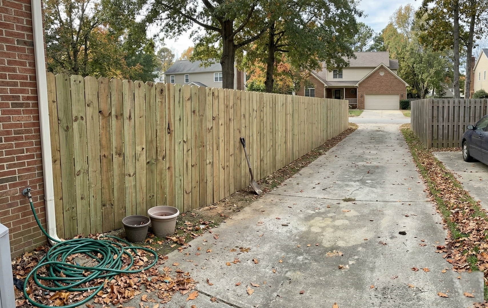 New dog-ear pressure-treated wood privacy fence along a residential driveway